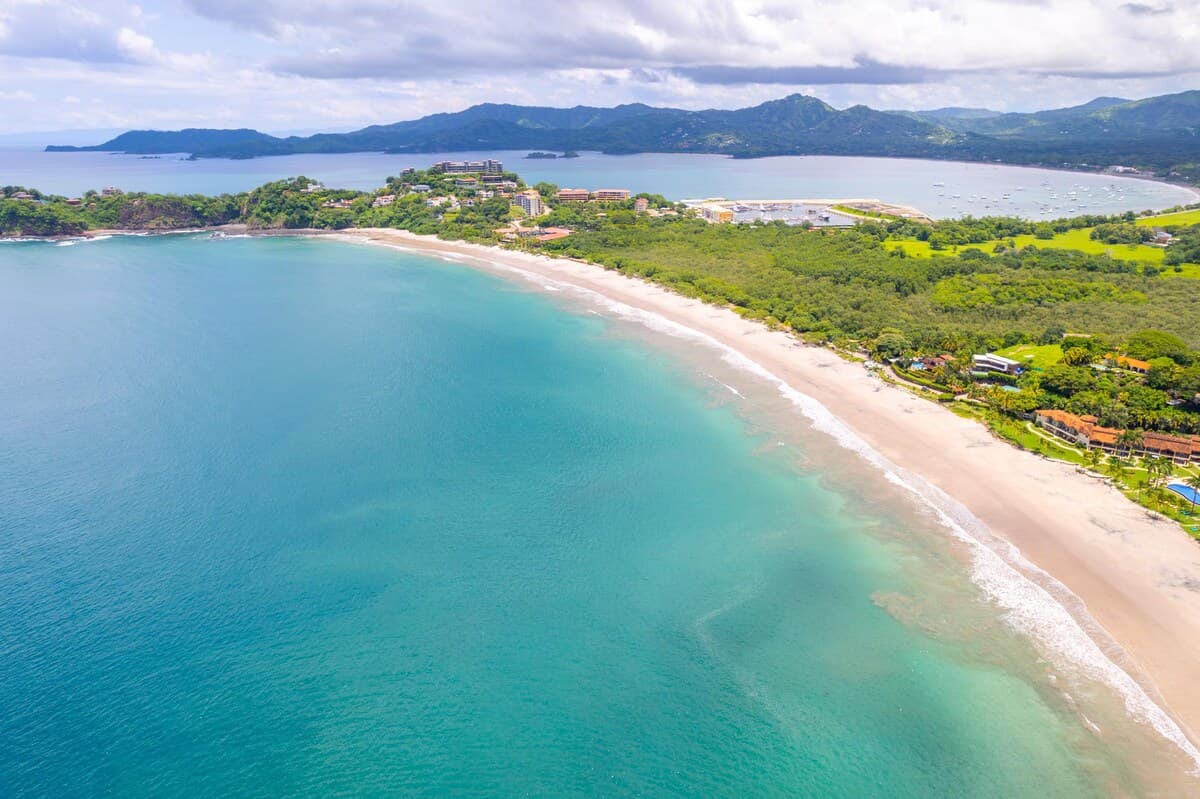 Aerial view of Playa Flamingo with turquoise water, white sand shoreline, and coastal hills in Guanacaste, Costa Rica
